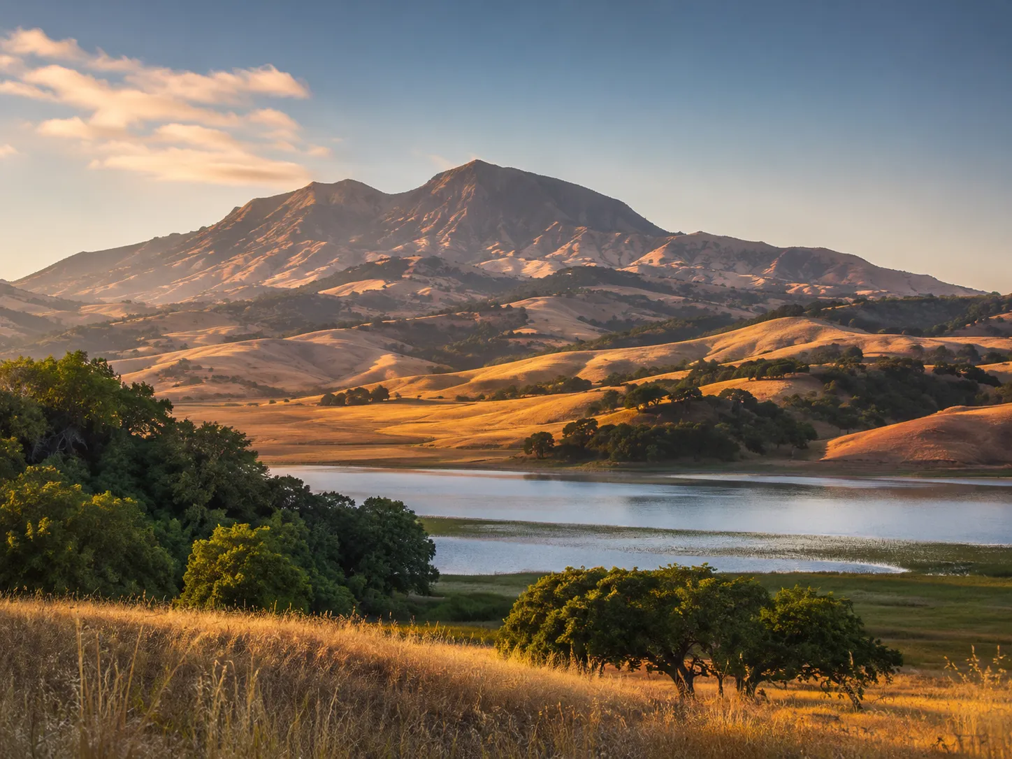 Golden-hour view of Mount Diablo above rolling golden hills, oak trees, and a calm lake in Contra Costa County, California